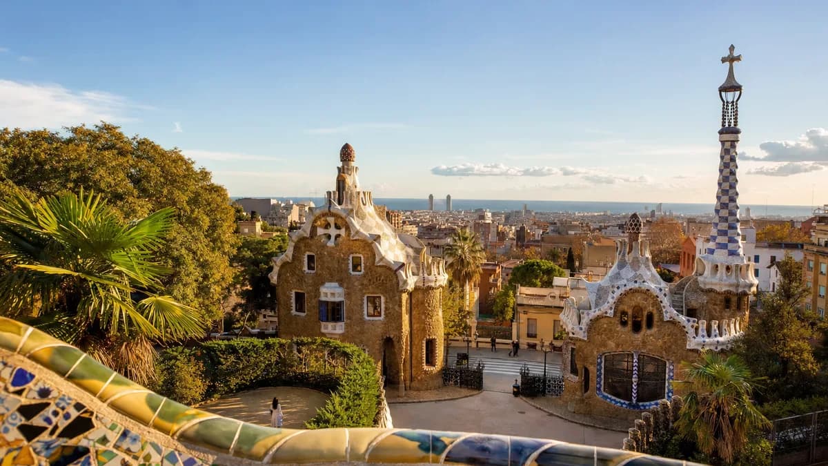 AI-generated image: Park Güell, Barcelona: A sunlit view of the vibrant mosaics and whimsical structures of Park Güell, surrounded by lush greenery. In the background, a few visitors stroll leisurely